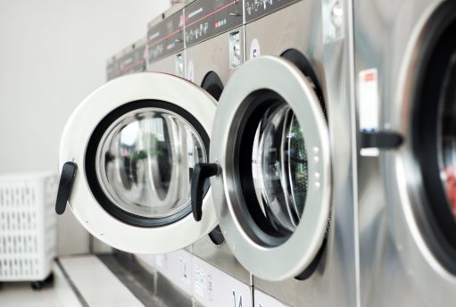 Selective focus on the front door of the washing machine with blurred close doors in foreground. Row of washing machines in the washing shop
